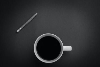 灰色的铅笔在黑色表面附近的白色陶瓷茶杯
